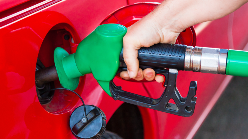 Mão enchendo tanque de carro vermelho.